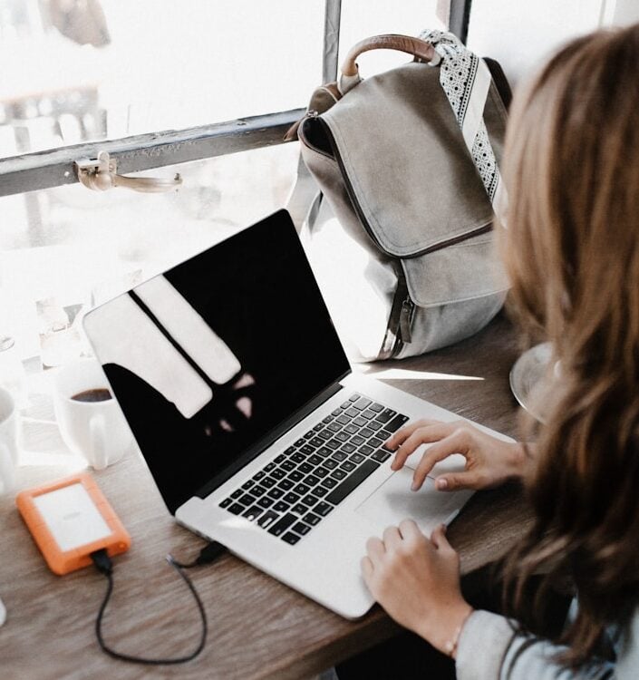 girl wearing grey long-sleeved shirt using MacBook Pro on brown wooden table